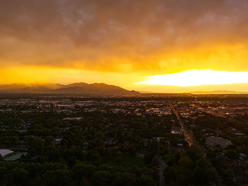 Salt Lake City spread out below an orange sunset sky, with mountains on the horizon.