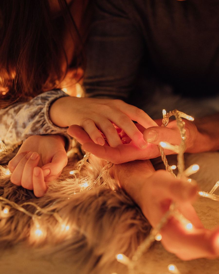 Two people's hands intertwined with warm glowing string lights.